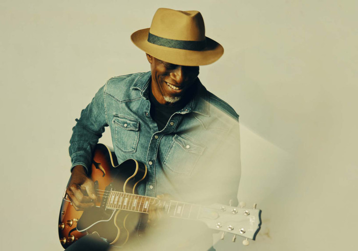 Man with hat in a blue shirt playing a guitar