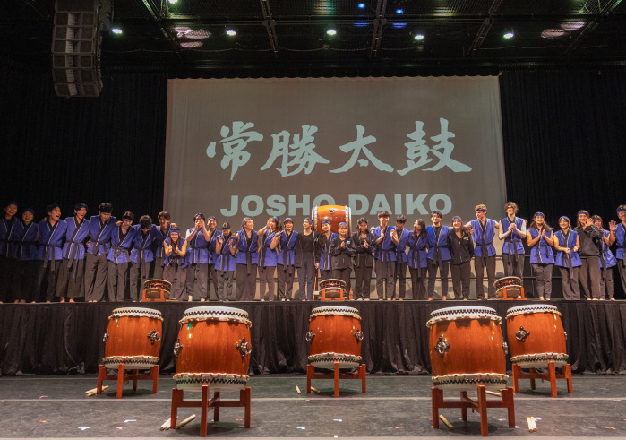 Drummers on a stage with a film in the background